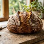 A freshly baked sourdough loaf with a deeply golden, cracked crust and a dusting of flour.