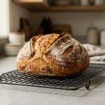 A freshly baked loaf of gluten-free sourdough bread on a cooling rack.